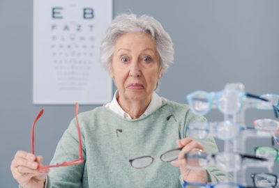 Senior woman choosing glasses at the eyewear shop, she is confused and pensive