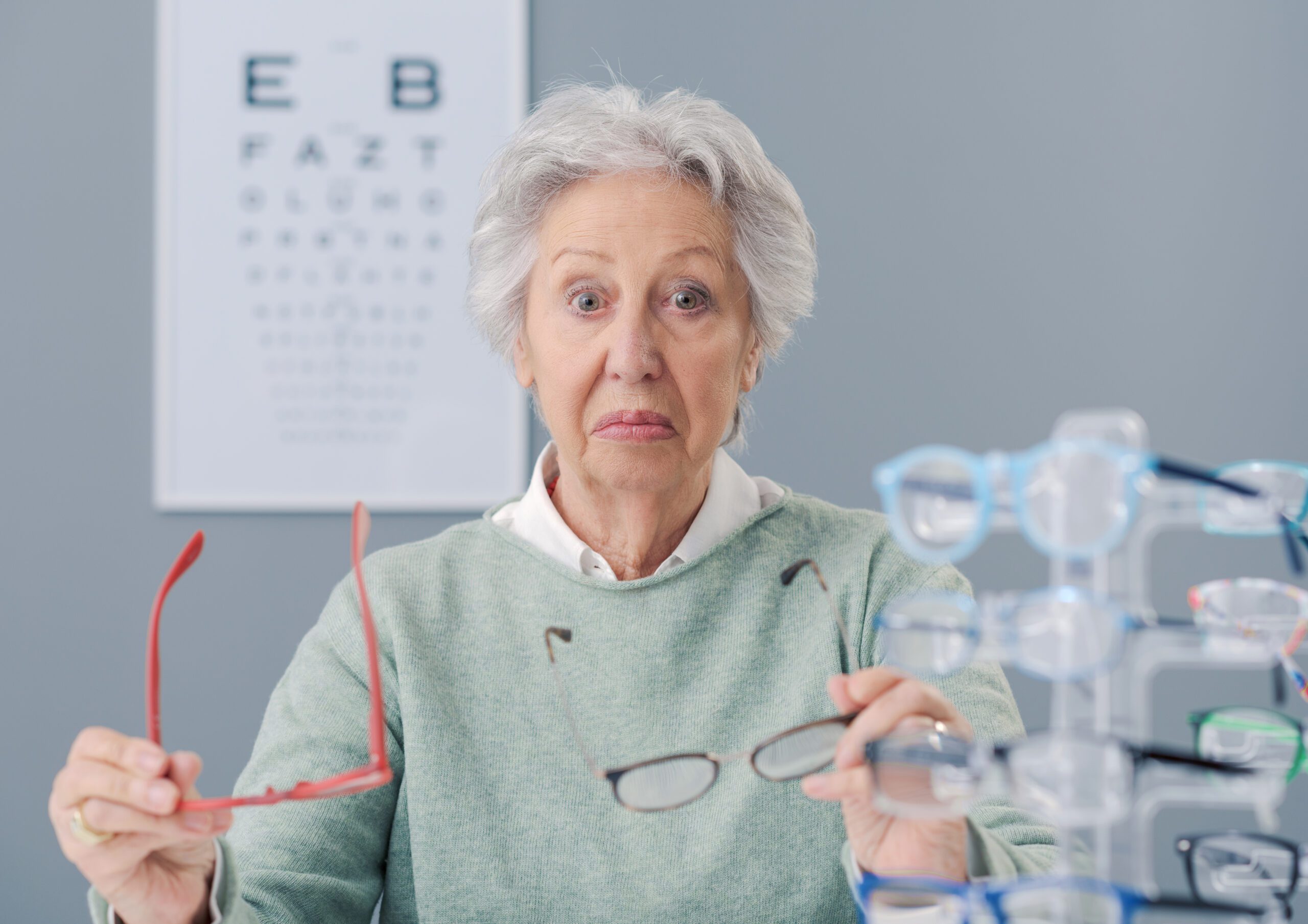 Senior woman choosing glasses at the eyewear shop, she is confused and pensive